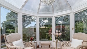 Une véranda meublée de mobilier en osier, agrémentée d’un lustre et offrant une vue sur le jardin.