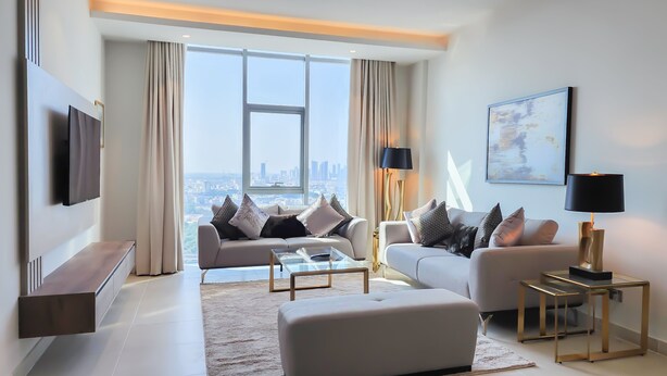 A modern living room with a sofa, ottoman, coffee table, and a TV mounted on the wall. - FARHAN TOWER (Manama)