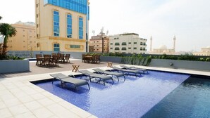 A rooftop swimming pool with lounge chairs and a view of city buildings. - FARHAN TOWER (Manama)
