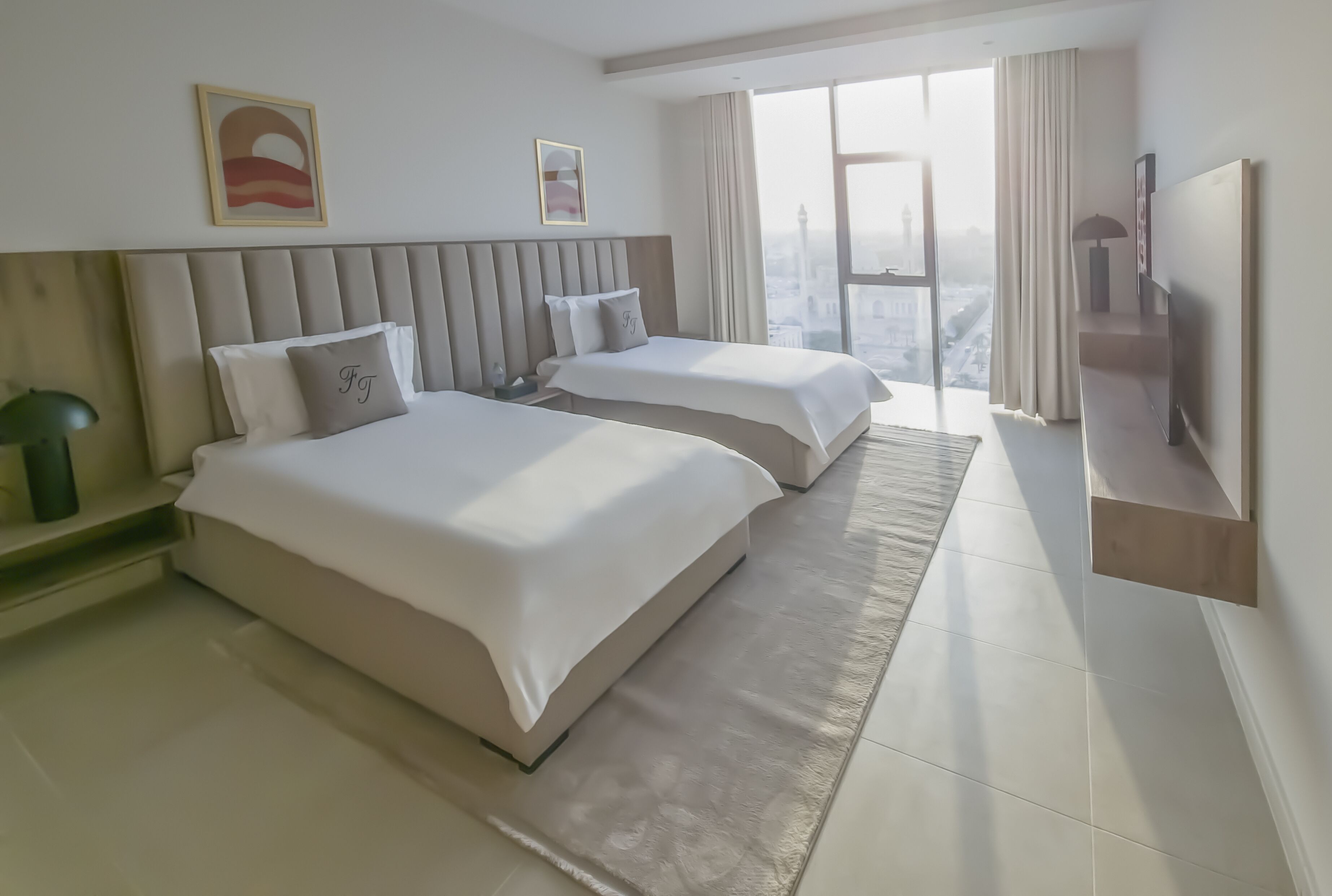 Una habitación de hotel moderna con dos camas, un ventanal con vistas a la ciudad y un televisor de pantalla plana montado en la pared.