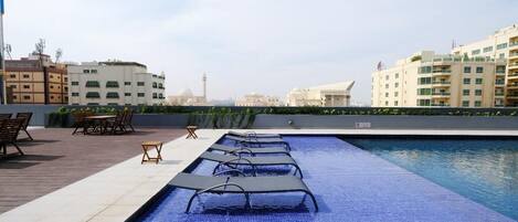 Un espace piscine aménagé sur le toit, avec des chaises longues et une vue sur les bâtiments environnants.