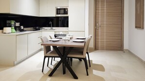 A modern kitchen with white cabinets, a microwave, and a dining area with a table set for four. - FARHAN TOWER (Manama)