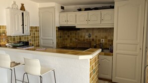 Een keuken met witte kasten, een betegelde spatwand en een centraal kookeiland met barstoelen.