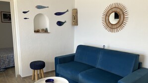 Un salon avec un canapé bleu, une petite table ronde sur laquelle sont posés des bols bleus, un miroir fixé au mur et des décorations murales représentant des poissons.
