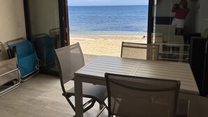 Une pièce avec une table et des chaises, une vue sur la plage par une porte ouverte, et une personne prenant une photo.
