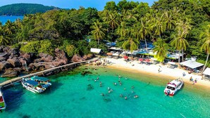 A beach with clear turquoise water, palm trees, and a dock with boats. - La Palma Hotel & Spa Sunset Town Phu Quoc (Phu Quoc)