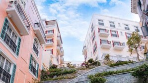 A person in a pink dress walking down a curved staircase with metal railings, surrounded by greenery and buildings with balconies. - La Palma Hotel & Spa Sunset Town Phu Quoc (Phu Quoc)