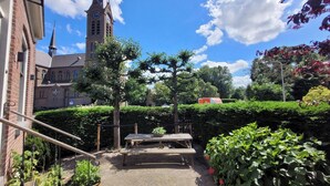 A courtyard with a church, a clock tower, and a picnic table surrounded by greenery.
