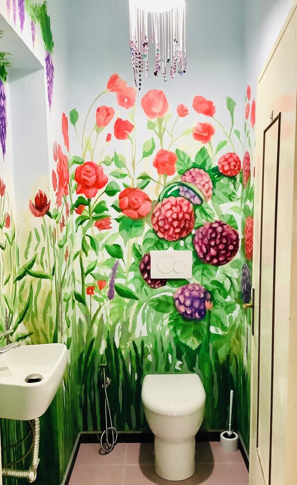 Un baño con un mural floral en la pared, un inodoro, un lavabo y una lámpara colgante.