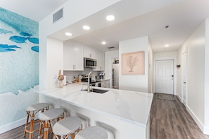 Una cocina moderna con armarios blancos, una isla central con taburetes, microondas y un fregadero.