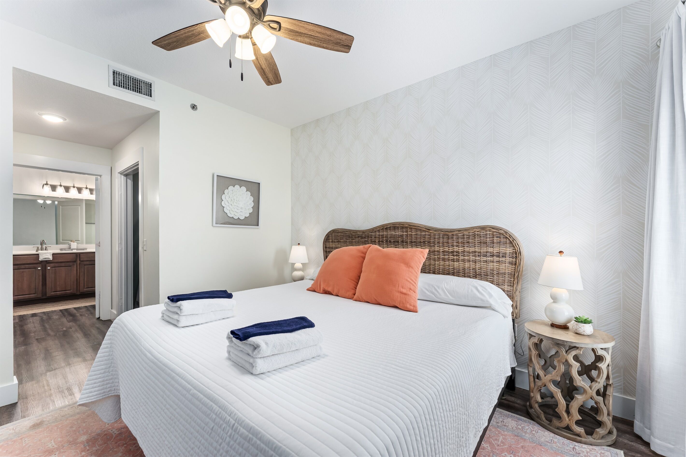 Hotelkamer met een groot bed, een plafondventilator, een nachtkastje met lamp en een badkamer door een geopende deur zichtbaar.