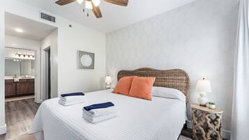 Hotelkamer met een groot bed, een plafondventilator, een nachtkastje met lamp en een badkamer door een geopende deur zichtbaar.