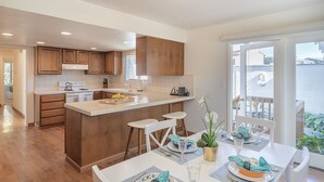 Cocina moderna con armarios de madera, una isla central y un comedor con sillas blancas y una mesa para dos.
