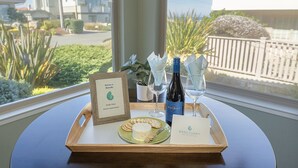 Una bandeja con una tabla de quesos, copas de vino, una botella de vino, un cartel de bienvenida enmarcado y una tarjeta sobre una mesa junto a una ventana.