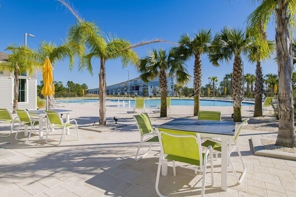 Un espace extérieur avec une piscine, des chaises longues et des tables, le tout entouré de palmiers.