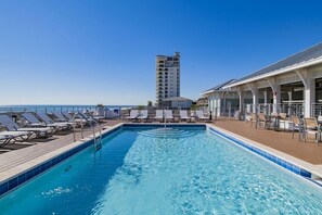 Piscina com espreguiçadeiras e um edifício ao fundo.