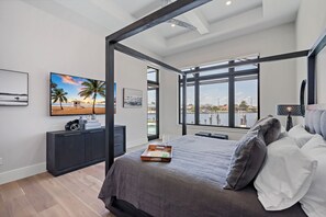 A bedroom with a large bed, a nightstand, a TV, and a window with a view of a marina.