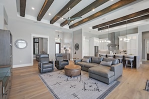 A spacious living room with a large gray sectional sofa, a round ottoman, and a patterned rug.