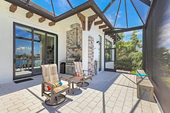 A covered patio with outdoor furniture, a grill, and a view of the surrounding landscape.