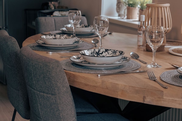 Une table à manger dressée avec des assiettes, des bols, des couverts et des verres, entourée de chaises à revêtement gris.