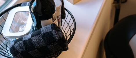 A kitchen counter with a bottle of wine, a basket with a cloth, and a wooden utensil holder.