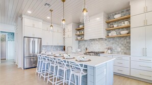 Una cocina moderna con armarios blancos, una isla central con taburetes de bar e iluminación colgante.