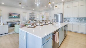 Una cocina moderna con una isla grande, armarios blancos e iluminación colgante.