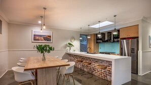Et moderne køkken med en central ø, hvide barstole og en hængende lampe.