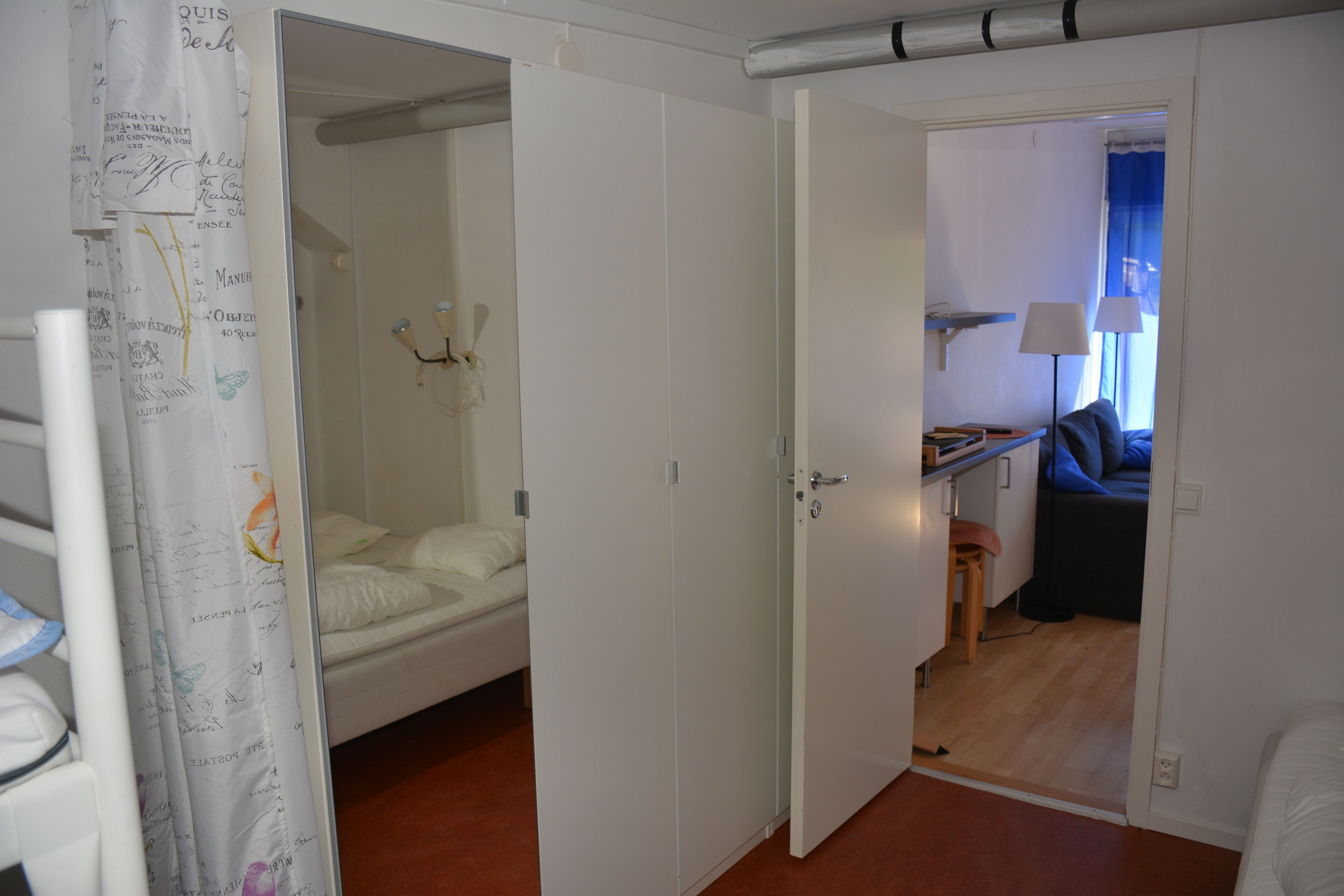 Una habitación con una cama, un escritorio y una silla. Hay una puerta que da a otra habitación.