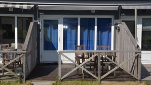A wooden deck with a table and chairs, a covered entrance, and a view of the surrounding area.