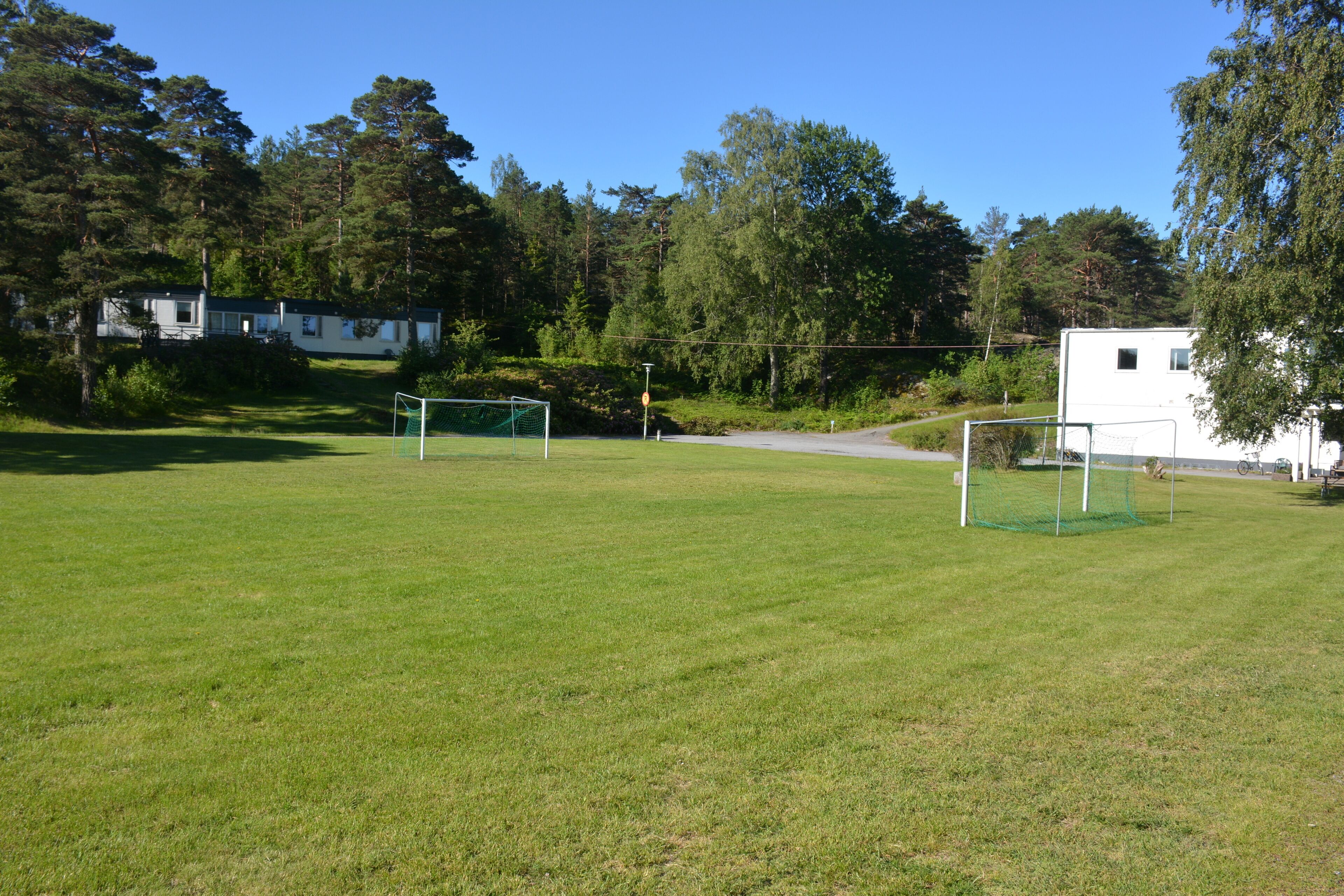 Un terrain herbeux avec deux buts de football, entouré d’arbres et de quelques bâtiments.