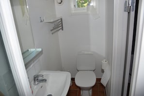 A small, clean bathroom with a white sink, toilet, and a small window above the toilet.