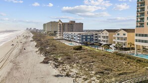 A beachfront hotel with multiple buildings, a sandy beach, and a clear sky. - Cozy, comfortable and freshly renovated oceanfront condo...you're gonna love it! (North Myrtle Beach)