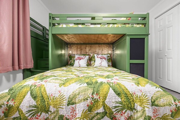 A bunk bed with a green frame, a floral quilt, and two pillows with flamingo designs.