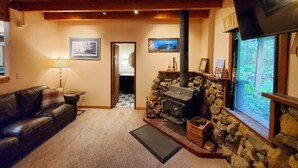 A cozy living room with a stone fireplace, a television mounted on the wall, and a comfortable couch. - Rustic Cabin & A-Frame w/ Firepit (Juneau)
