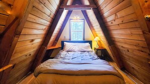 A cozy attic bedroom with a sloped ceiling, a single bed, a nightstand, and a window providing natural light. - Rustic Cabin & A-Frame w/ Firepit (Juneau)