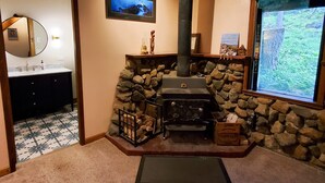 A bathroom with a stone wall, a fireplace, and a window with a view of trees. - Rustic Cabin & A-Frame w/ Firepit (Juneau)