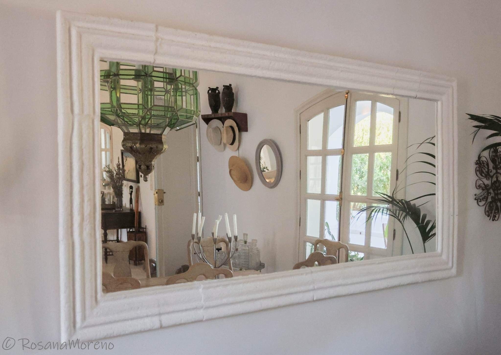 A room with a large mirror reflecting a window, a chandelier, and various decorative items.