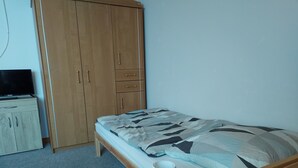 A bedroom with a bed, a wooden wardrobe, a television on a cabinet, and a lamp on a bedside table. - Appartement Ottermeet (Ihlow)