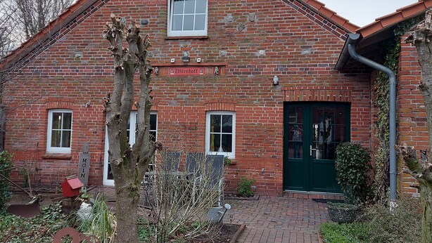 A brick building with a green door, a window, and a sign that reads "Moin". - Appartement Ottermeet (Ihlow)