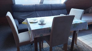 A cozy room with a dark grey sofa, a small dining table with a white tablecloth, and two chairs. - Appartement Ottermeet (Ihlow)