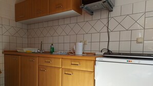 A kitchen with wooden cabinets, a white refrigerator, and a tiled backsplash. - Appartement Ottermeet (Ihlow)