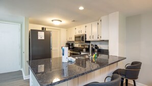 Una cucina moderna con ripiani in granito, elettrodomestici in acciaio inossidabile e un'area bar con due sgabelli.