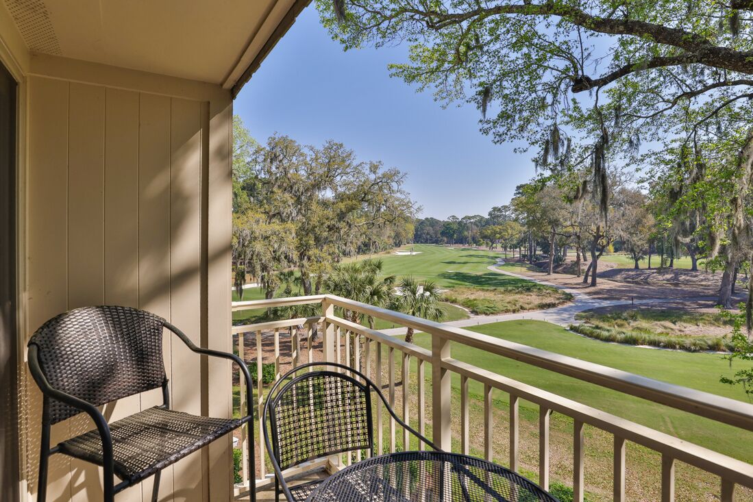 A balcony with two wicker chairs overlooking a golf course.