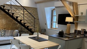 A modern kitchen with a dining area, featuring a wooden staircase, a large window, and a built-in TV. - Appartement avec terrasse & parking Sarlat Centre (Sarlat-la-Canéda)
