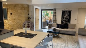 A modern living room with a sofa, a dining table with chairs, and a kitchen area with a stone wall. - Appartement avec terrasse & parking Sarlat Centre (Sarlat-la-Canéda)