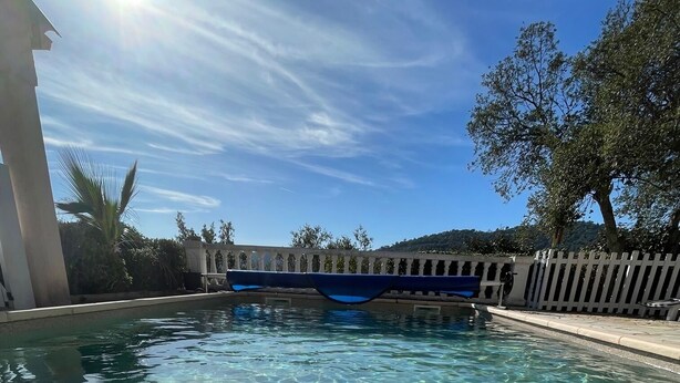 Ein klares Schwimmbecken mit einer Brücke im Hintergrund, umgeben von einem weißen Zaun und Bäumen.