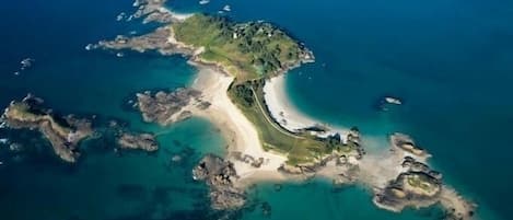 An aerial view of a coastal island with a sandy beach, rocky outcrops, and clear blue waters.