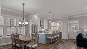 Una cocina amplia con armarios blancos, una isla central y un comedor con sillas de madera.