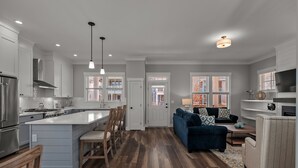 Una cocina moderna con armarios blancos, una isla central y un comedor con sillas de madera.